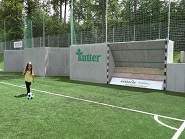 Kleines Mädchen kickt vergnügt an einer Kickbacks Fußballwand.